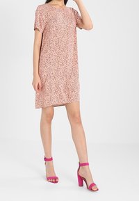 Růžové šaty s krátkým rukávem a rozptýleným potiskem, s volným střihem. Doplněné o růžové sandály na vysokém podpatku s kotníkovými pásky.