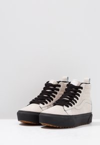 Hochschuhsneaker aus hellbeigem Wildleder mit schwarzen Schnürsenkeln, Gummisohle und einer strukturierten schwarzen Plattform. Verstärkte Ösen und Nähte.
