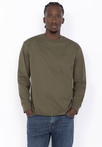 Sweatshirt vert olive à manches longues en coton, avec un col rond et des poignets cousus, associé à un jean en denim bleu.