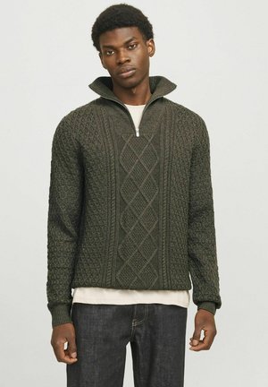 Donkergroene gebreide trui met een hoge kraag en een halve rits. Heeft textuurelementen en een gelaagd uiterlijk over een licht shirt.
