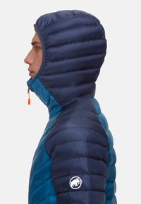 Dunkelblaue Daunenjacke mit Kapuze, glänzender Oberfläche und Zickzacknähten. Mit oranger Reißverschluss-Zuglasche und weißem Logo auf dem Ärmel.