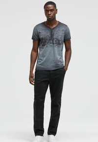 Gray short-sleeve shirt with a faded texture and printed graphics, paired with black pants and white sneakers. Casual attire.