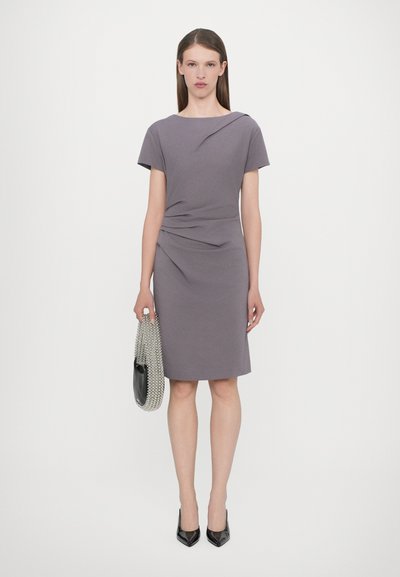 Fitted gray dress with short sleeves, draped design at the waist, knee-length hem, paired with a beaded handbag and black pointed heels.