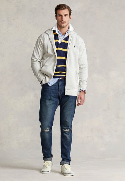 Ljusgrå zip-up-hoodie, marinblå och gula randiga pikétröja, ljusblå skjorta med knappar, slitna blå jeans och vita sneakers.