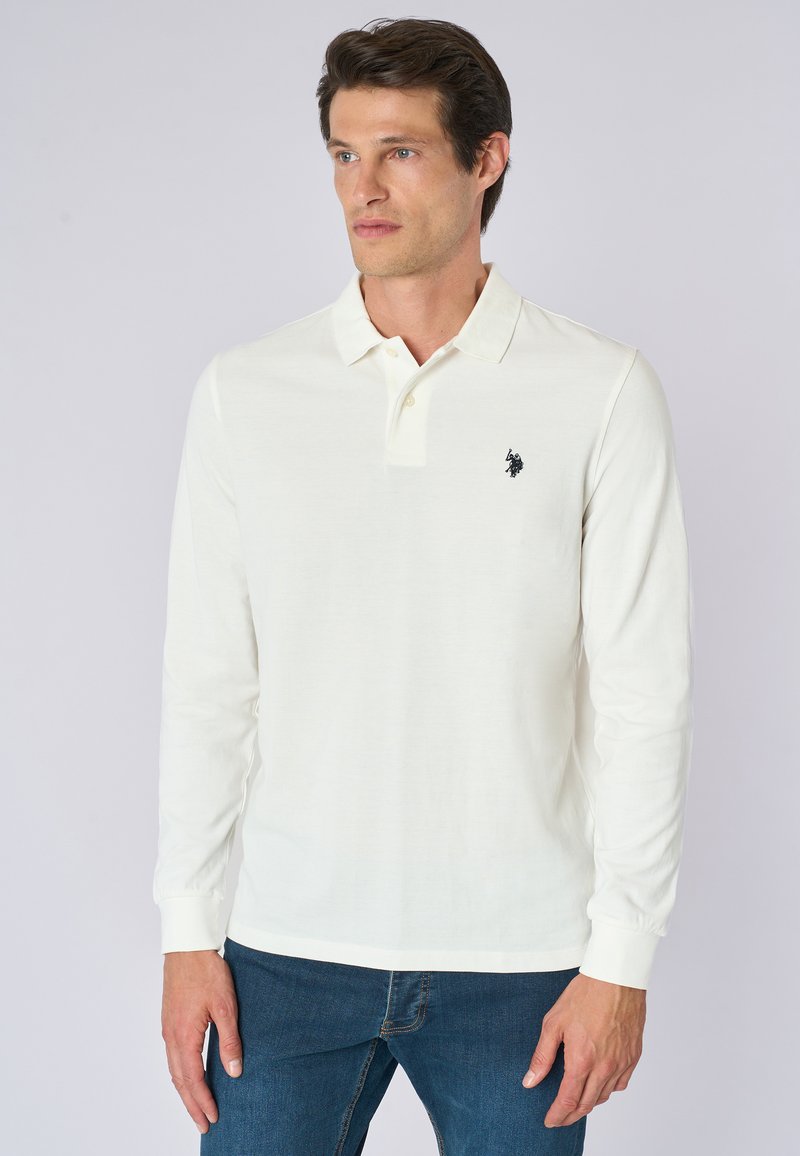 Polo a maniche lunghe bianco realizzato in tessuto morbido, con colletto classico, patta con tre bottoni e un piccolo logo nero sul petto.