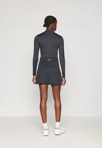 Top preto de mangas longas combinado com uma saia preta canelada. O conjunto apresenta um design ajustado, textura suave e um detalhe de logotipo na cinta.