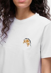 Witte katoenen t-shirt met een kleine, geborduurde bruine en beige croissant in zwarte draad. Korte mouwen en een ronde hals.