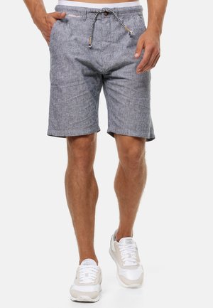 Shorts rayés gris et blanc avec une taille à cordon de serrage, des poches latérales et des ourlets roulés, fabriqués en tissu léger. Portés avec des baskets blanches.