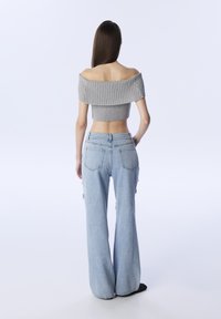 Šedý crop top s odkrytémi rameny a žebrovaným vzorem v kombinaci s světle modrými širokými džíny s bočními kapsami a volným střihem.