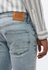 Σκούρα μπλε τζιν από τζιν ύφασμα με δερμάτινη ετικέτα Scotch & Soda Amsterdam στη ζώνη μέσης και πολύχρωμες ραφές κοντά στην άκρη της πίσω τσέπης.