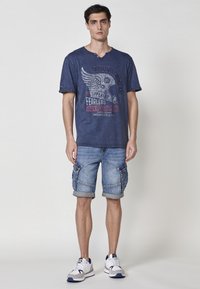 Mornarska grafična majica s kratkimi rokavi in okroglim izrezom, kombinirana z denim kratkimi hlačami s stranskimi žepi in zavihki.