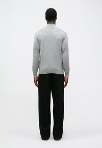 Pulover tricotat de culoare gri deschis, cu un design cu guler, mansete ajustate și o margine dreaptă, asortat cu pantaloni largi negri. Textură netedă, detalii minime.