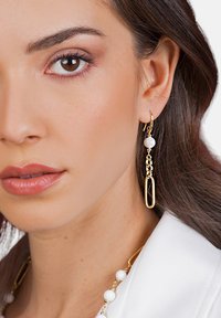 Pendientes colgantes en tono dorado que presentan una perla redonda blanca y un diseño de eslabón ovalado texturizado, destacando un estilo moderno y elegante.