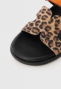 Leopard print fabric strap sandal with a black textured sole and orange accent. Features a cut-out design on the strap for breathability.