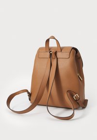 Sac à dos en cuir brun avec une finition texturée, doté d'une poignée supérieure, de sangles réglables et d'une fermeture éclair dorée. Design simple et fonctionnel.