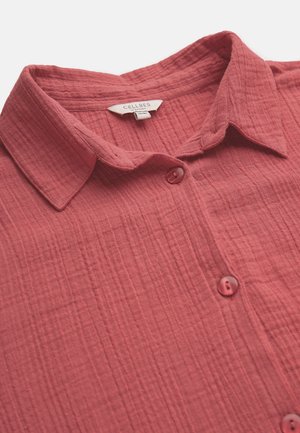 Rotes, strukturiertes Hemd mit Knopfleiste, Kragen und Etikett mit der Aufschrift "Cellbes of Sweden", Nahaufnahme vor weißem Hintergrund.