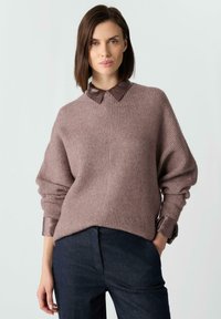 Jasnobrązowy prążkowany sweter z brązowym skórzanym kołnierzem, opuszczonymi ramionami i szerokimi rękawami, zestawiony z ciemnoniebieskimi spodniami.