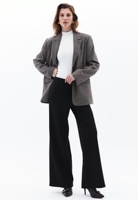 Blazer grigio oversize, top bianco a collo alto, pantaloni neri a gamba larga, scarpe nere con tacco. Il blazer ha un colletto a punta e chiusura con bottoni.