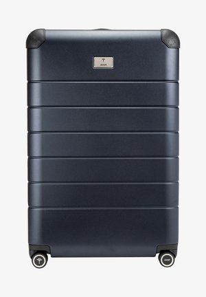 Valise rigide marine avec des rainures verticales, des protecteurs d'angle en caoutchouc, quatre roues noires et un logo argenté à l'avant.