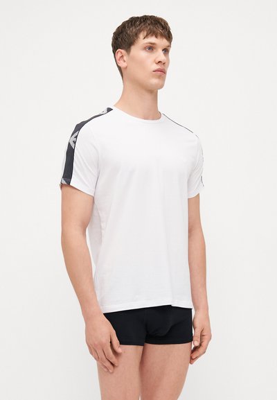 White t-shirt with black striped accents on shoulders, short sleeves, round neck, made of lightweight fabric, paired with black shorts.