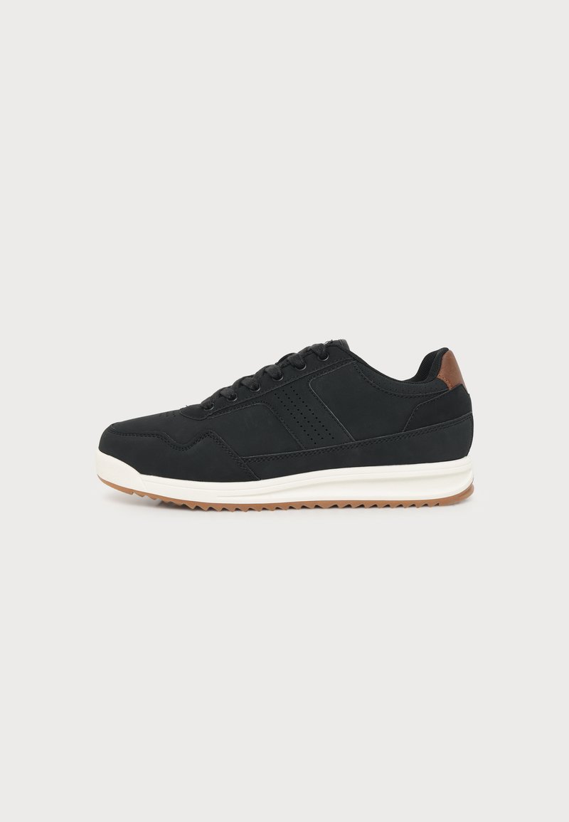 Μαύρο χαμηλό sneaker με κορδόνια μπροστά, λευκή σόλα και καφέ λεπτομέρεια στη φτέρνα, σε απλό ανοιχτό φόντο.