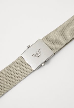 Beige woven fabric belt with a metallic rectangular buckle featuring a logo. Textured surface and smooth edges enhance the design.