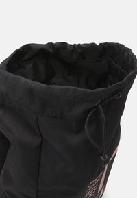 Svart tyg dragsko-väska med snörning och synlig inredning, delvis öppen mot en vit bakgrund.