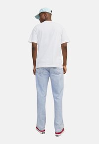 Camiseta blanca de manga corta, gorra azul clara, vaqueros azul claros, zapatillas de cuadros rojas, vista desde atrás, sobre un fondo blanco sencillo.