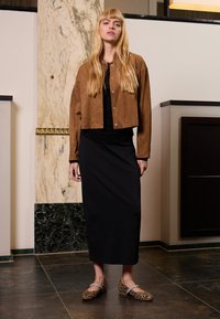 Suede brun cropped jakke med trykknapper, lagd over en svart kjole. Leopardmønstrede lave hæler. Marmor bakgrunn.
