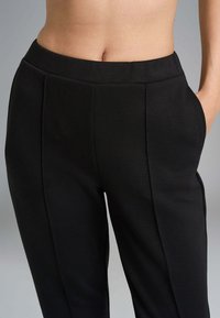 Pantaloni neri con una trama liscia, dotati di una vita ampia, tasche laterali e pieghe nette sulla parte frontale per un design strutturato.