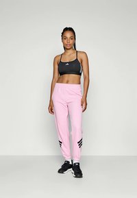 Svart sports-BH med tynne stropper og hvite striper, kombinert med lyse rosa joggebukser med svarte tre-striper og elastiske mansjetter.