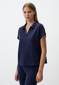 Marineblauw T-shirt met korte mouwen en een V-hals, met een ontspannen pasvorm en een zachte textuur. Eenvoudig ontwerp met opgerolde mouwen, gecombineerd met bijpassende broek.