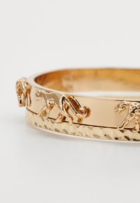 Bracelet en or avec des gravures de léopard, présentant un bandeau martelé texturé et une surface lisse et polie en forme circulaire.