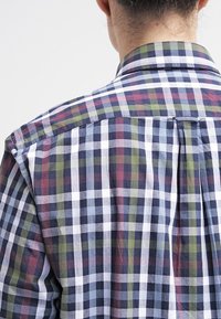 Karierte Hemd in einer Mischung aus Marineblau, Weiß, Burgund und Grün. Der Stoff wirkt leicht und hat eine lockere Passform sowie einen Rückenschlitz.