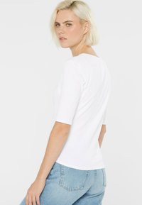 Weißes, geripptes T-Shirt mit kurzen Ärmeln, rundem Ausschnitt und taillierter Form. Kombiniert mit hellblauen Jeans für einen lässigen Look.