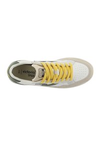 Zapatilla blanca con cordones amarillos, detalles verdes y puntera perforada. Presenta una entresuela beige y una etiqueta "victoria 1985" en la lengüeta.