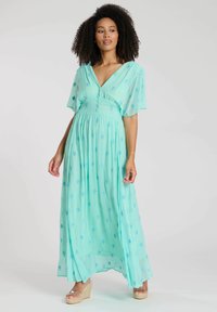 Ljus turkos maxiklänning med korta fladderärmar, knappar och dekorativ blå broderi över hela tyget.