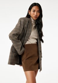 Brunternet blazer med strukturerede skuldre, parret med en cremefarvet turtleneck og en brun mini nederdel. Glat tekstur, skræddersyet pasform.