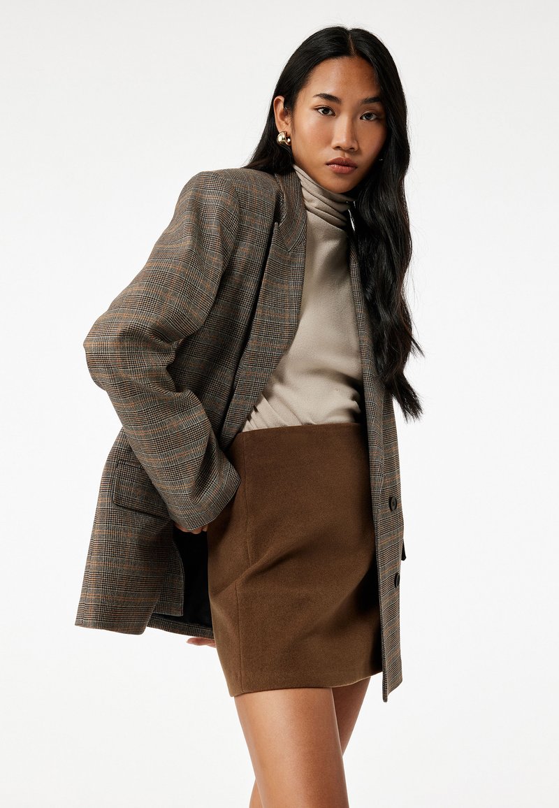 Brunternet blazer med strukturerede skuldre, parret med en cremefarvet turtleneck og en brun mini nederdel. Glat tekstur, skræddersyet pasform.