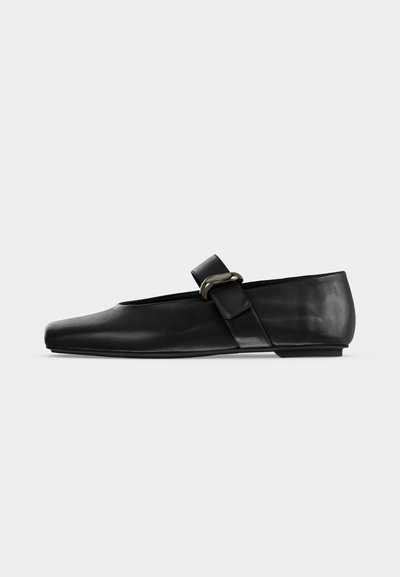 Chaussure plate en cuir noir avec un bout arrondi et une bride ornée d'une boucle métallique sur le cou-de-pied.