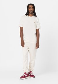 Camiseta crema de manga corta, con detalle de logo, combinada con joggers crema y zapatillas burdeos con acentos y cordones blancos.