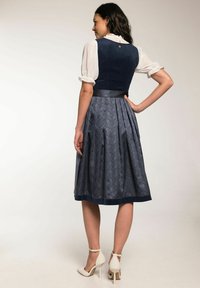 Navy-blaues traditionelles Kleid mit tailliertem Oberteil und plissiertem Rock, gefertigt aus gemustertem Stoff und einem satinband Gürtel, getragen mit cremefarbenen Absätzen.