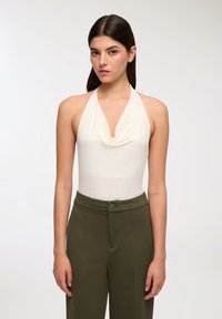 Body bianco con scollo a halterneck drappeggiato abbinato a pantaloni olive verdi a vita alta con bottone frontale e tasche laterali.