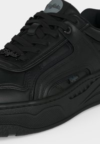 Baskets de la marque Black Buffalo en cuir, avec une semelle épaisse et texturée, des coutures détaillées et des lacets ornés d’un charme métallique avec le logo.