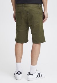 Olivgrüne Shorts aus Baumwollmischung mit Gesäßtaschen und dekorativer Stickerei, getragen mit weißen Sneakers und Knöchelsocken.