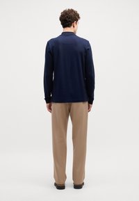 Polo de manga longa azul-marinho com um design texturizado, apresentando um colarinho plano e detalhe na pala traseira, combinado com calças bege e sapatos escuros.