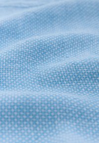 Lyseblåt vævet stof med et struktureret mønster af små, krydsende tråde, der skaber et blødt, tredimensionelt udseende.