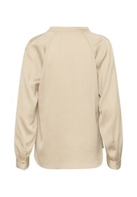 Beige langærmet skjorte, tekstureret stof med en rund kant, raglanærmer og knaplukning ved manchetterne. Bagansigt uden mønstre.
