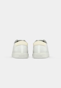 Pair of white low-top sneakers with beige heel accents, viewed from the back against a plain light background.