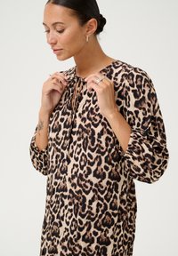 Blouse en imprimé léopard beige avec des accents noirs, dotée d'un col en clé avec un lien et de longues manches bouffantes avec des poignets élastiques.